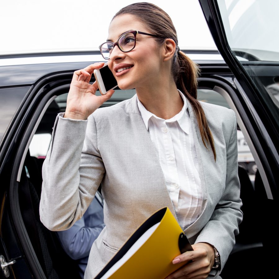 Young businesswoman talking on phone while as she exits the car.